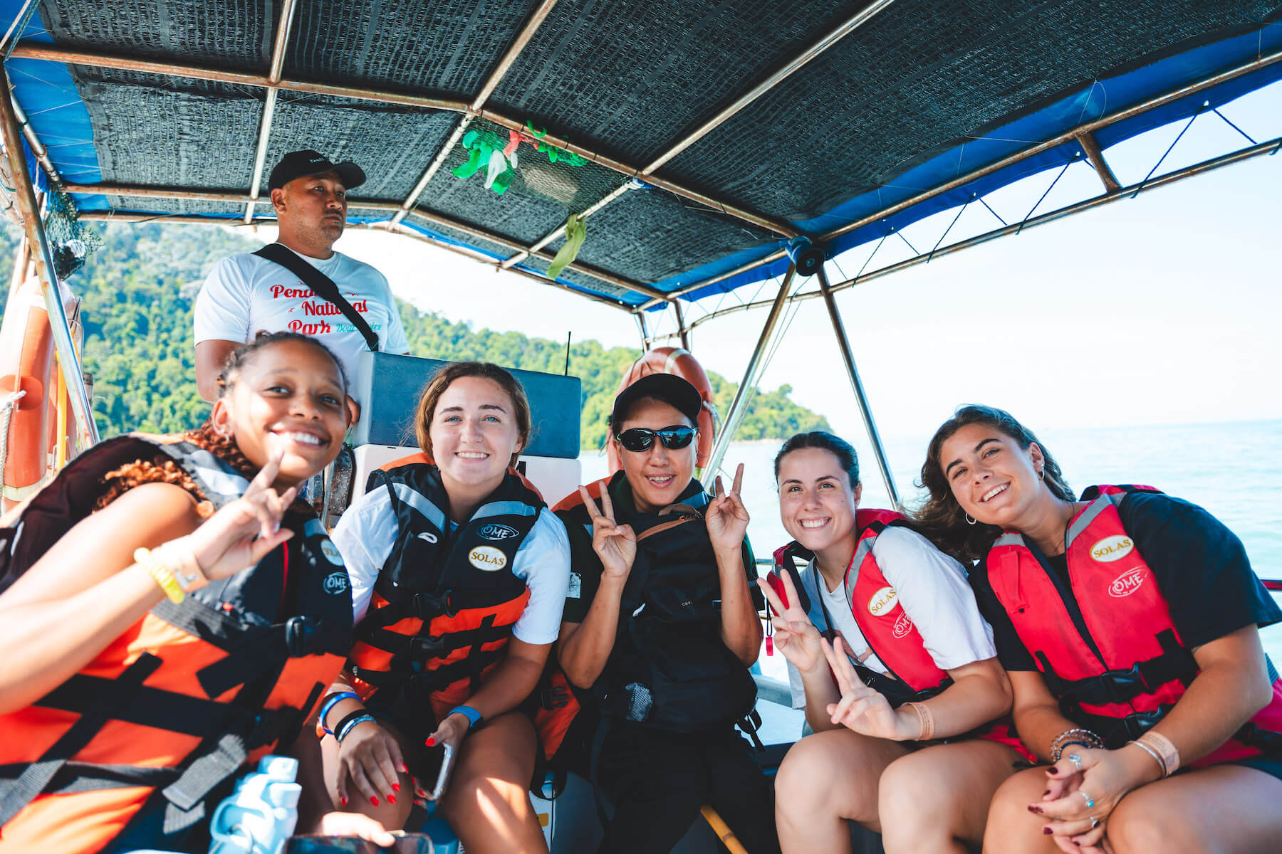 5 students on a boat wearing life vests smile at the camera.