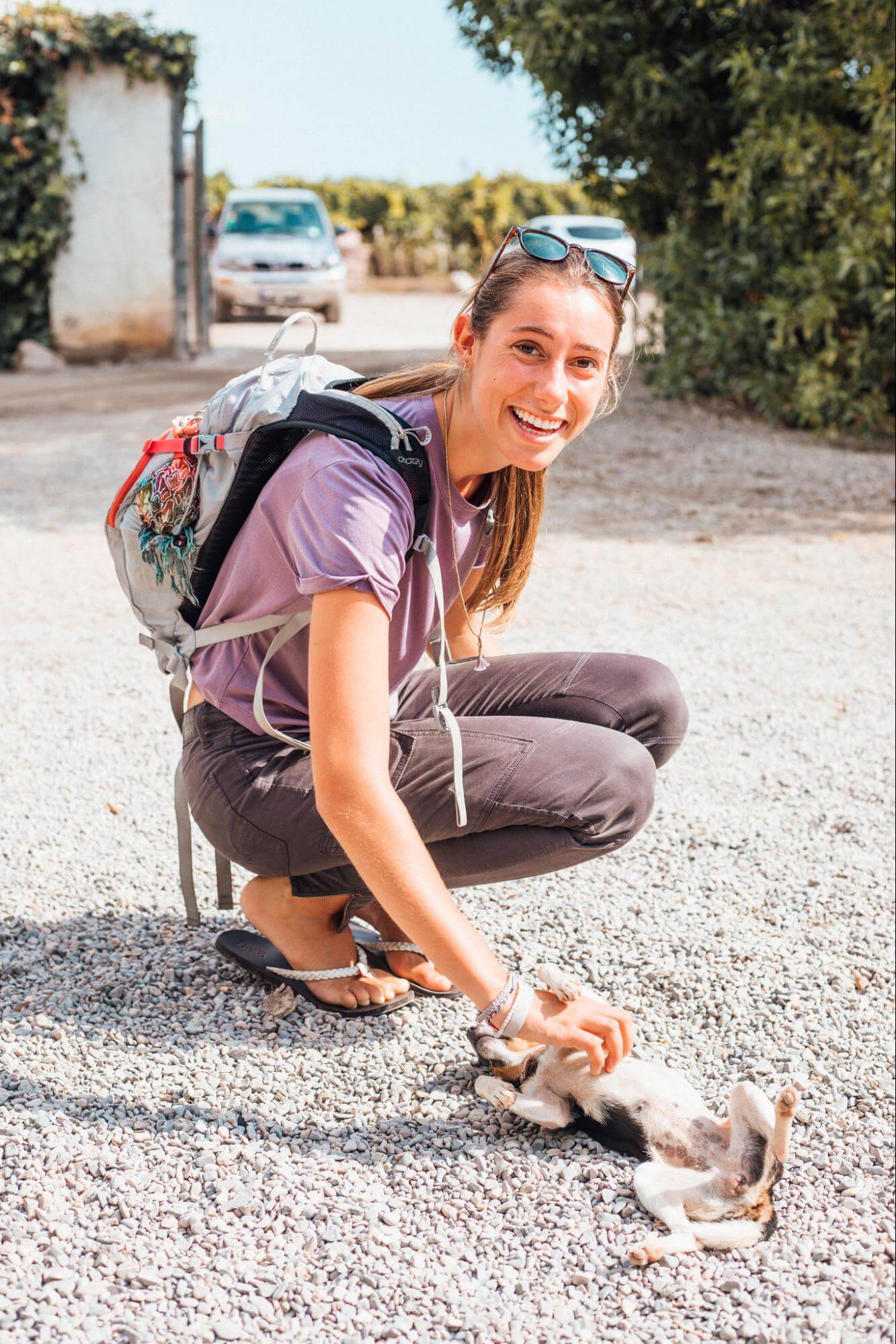 A young woman smiles at the camera as she crouches and scratches a small dog on the stomach.